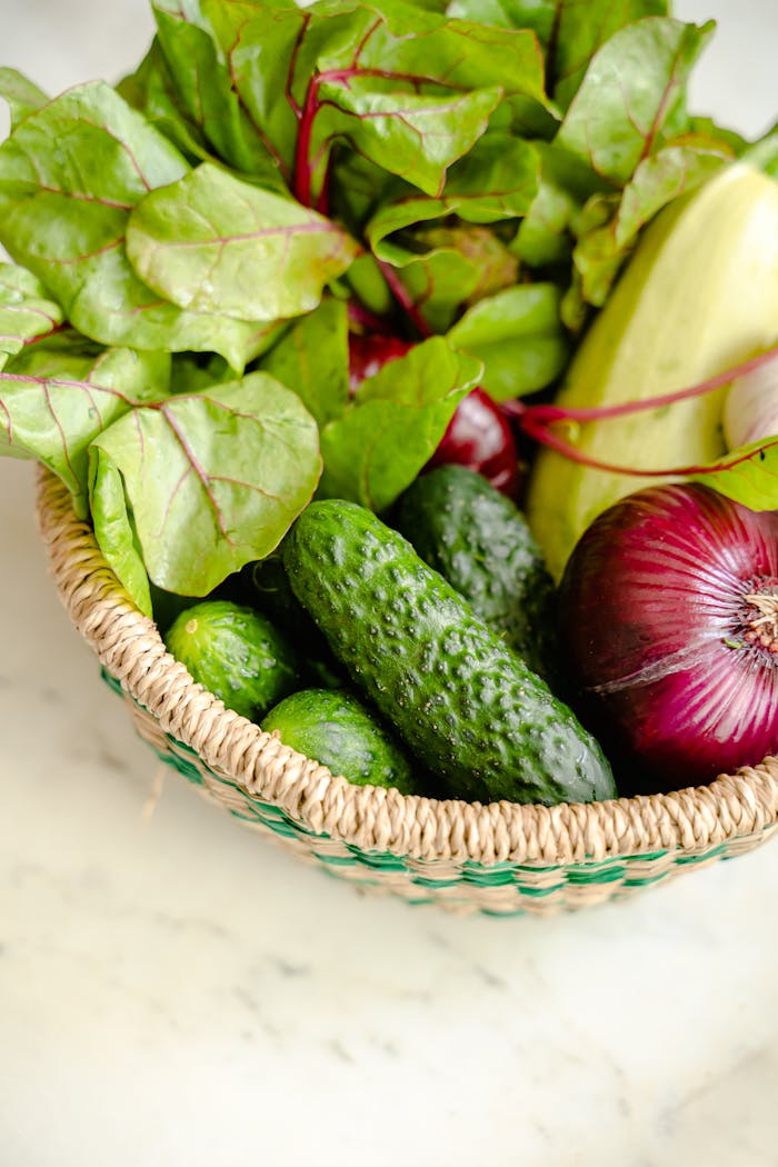 A vibrant display of fresh vegetables including cucumbers, onions, and greens in a woven basket.